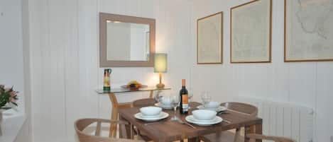 A dining area with a wooden table, chairs, a mirror, and framed artwork on the wall.