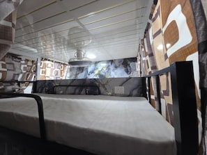 A room with a bed, a ceiling fan, and patterned walls. - Nithyanand Male Cabinstay dormitory (Mumbai)