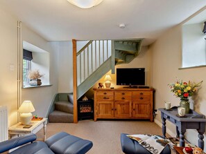 A living room with a fireplace, a TV, a wooden cabinet, and a staircase. - 1 Bed in Bridport (oc-37351) (Bothenhampton)