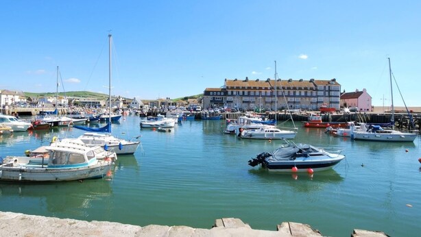 A marina with multiple boats docked, a large building in the background, and a clear sky. - 1 Bed in Bridport (oc-37351) (Bothenhampton)