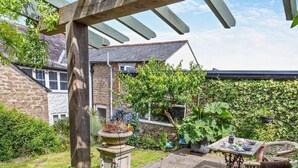 A garden with a pergola, a stone wall, and a table with chairs. - 1 Bed in Bridport (oc-37351) (Bothenhampton)