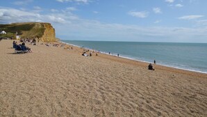 A beach with people, a cliff, and a flag. - 1 Bed in Bridport (oc-37351) (Bothenhampton)