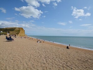 A beach with people, a cliff, and a flag. - 1 Bed in Bridport (oc-37351) (Bothenhampton)