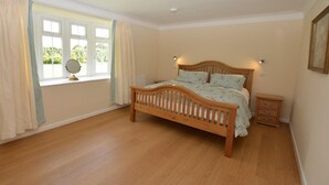 Une chambre à coucher avec un lit en bois, une fenêtre avec des rideaux, une table de chevet et une commode.