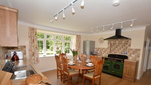 Une cuisine équipée d’une table à manger, de chaises, d’une cuisinière, d’un évier et d’une fenêtre avec des rideaux.