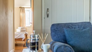 Une pièce avec un lit, un canapé bleu, une petite table avec une cafetière et une fenêtre avec des rideaux.