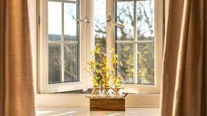Une fenêtre donnant sur des arbres, une boîte en bois avec des fleurs jaunes et des rideaux.