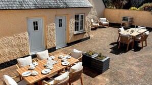 Une terrasse avec une table en bois dressée pour le repas, des chaises en osier et un mur en pierre.