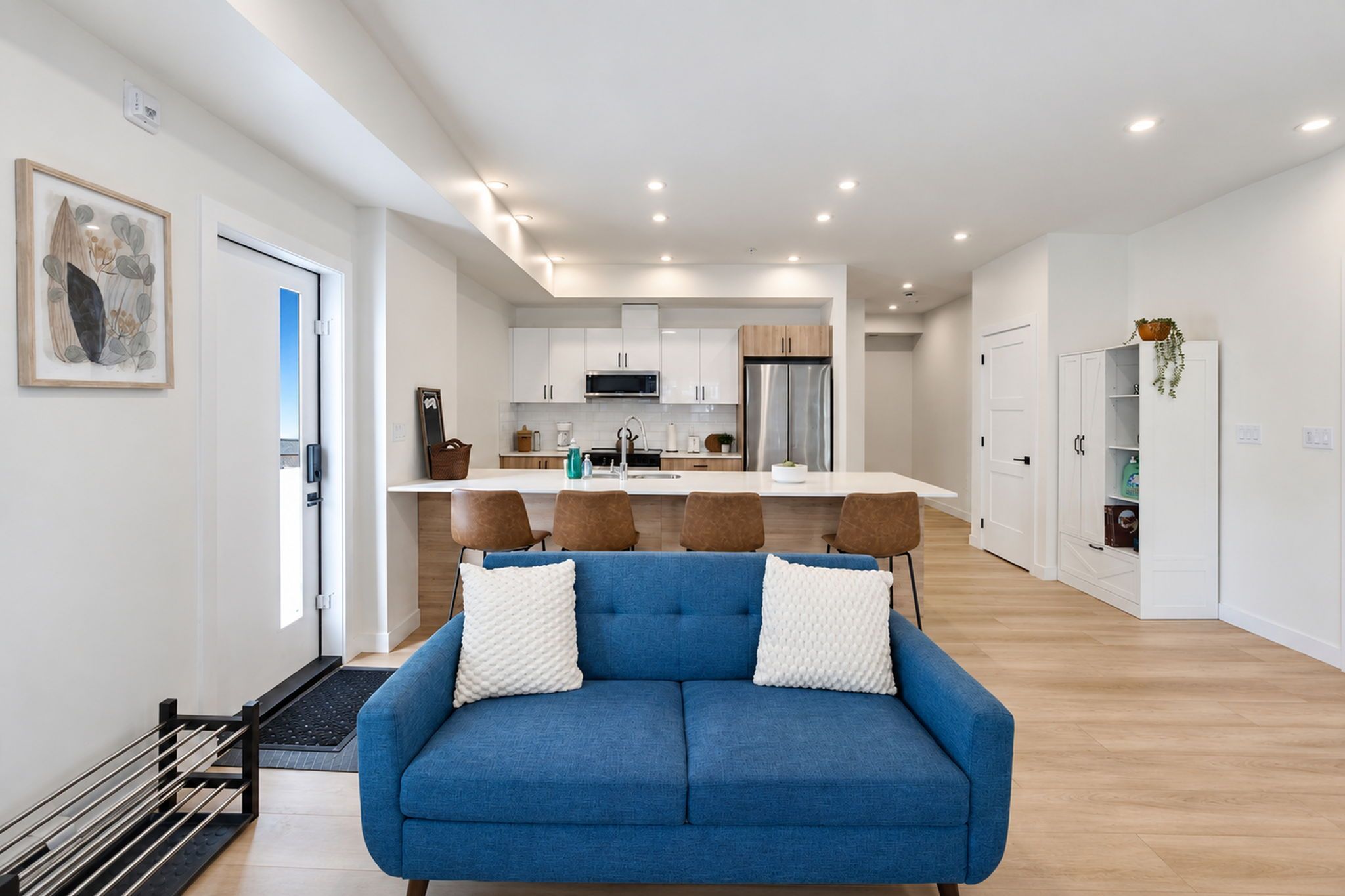 A modern living room with a blue sofa, a dining area with a white table, and a kitchen with white cabinets.