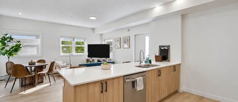 A modern kitchen with a central island, wooden cabinets, a dishwasher, and a dining area with chairs and a table.