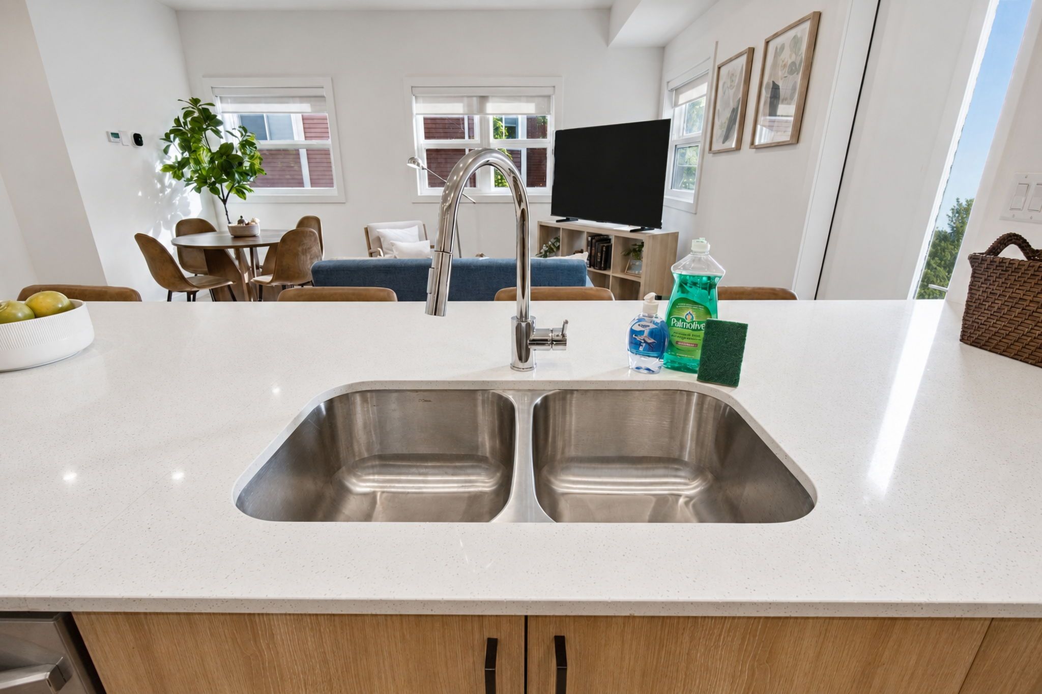 A modern kitchen with a double sink, a dining area with chairs, a television, and a plant.
