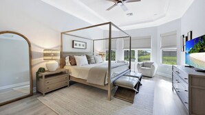Una camera da letto con un letto a baldacchino, una ventola a soffitto, uno specchio grande, una televisione e vista sull'esterno.