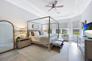 A bedroom with a four-poster bed, a ceiling fan, a large mirror, a television, and a view of the outdoors. - Esplanade by The Islands (Naples)