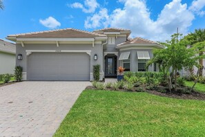A two-story house with a grey garage door, a small attached garage, and a well-maintained front yard with grass and shrubs. - Esplanade by The Islands (Naples)