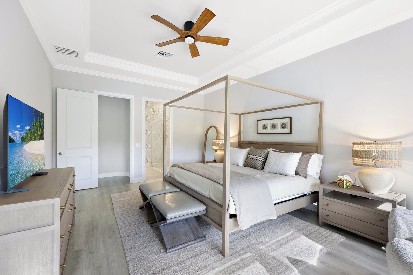 A modern bedroom with a four-poster bed, a ceiling fan, a television, and a nightstand with a lamp.