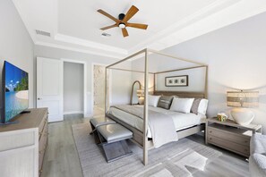 Quarto moderno com cama de dossel, ventilador de teto, televisão e mesa de cabeceira com abajur.