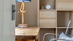Ett skrivbord i trä med en lampa, en stol och ett träskåp med en klocka och dekorativa föremål.