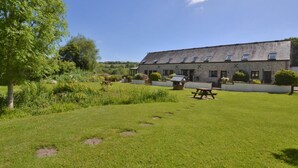 A rustic building with a flat roof, multiple windows, and a garden with picnic tables. - 1 Bed in Lyme Regis (oc-40483) (Lyme Regis)