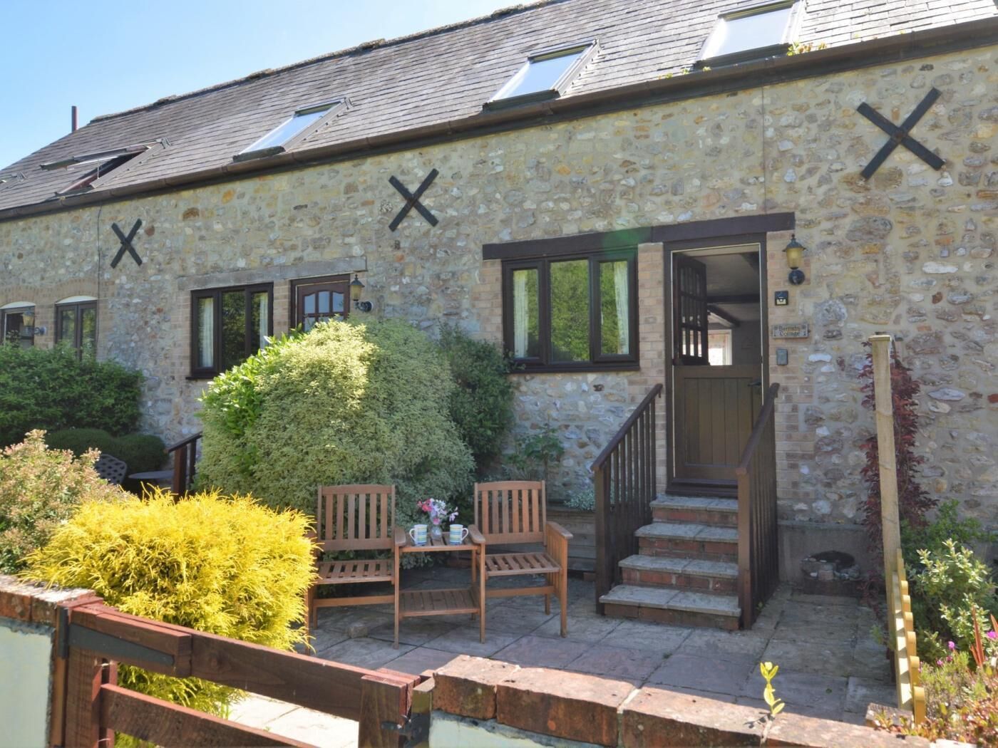 A stone building with a porch, two wooden chairs, a small table, and a staircase leading to an entrance.
