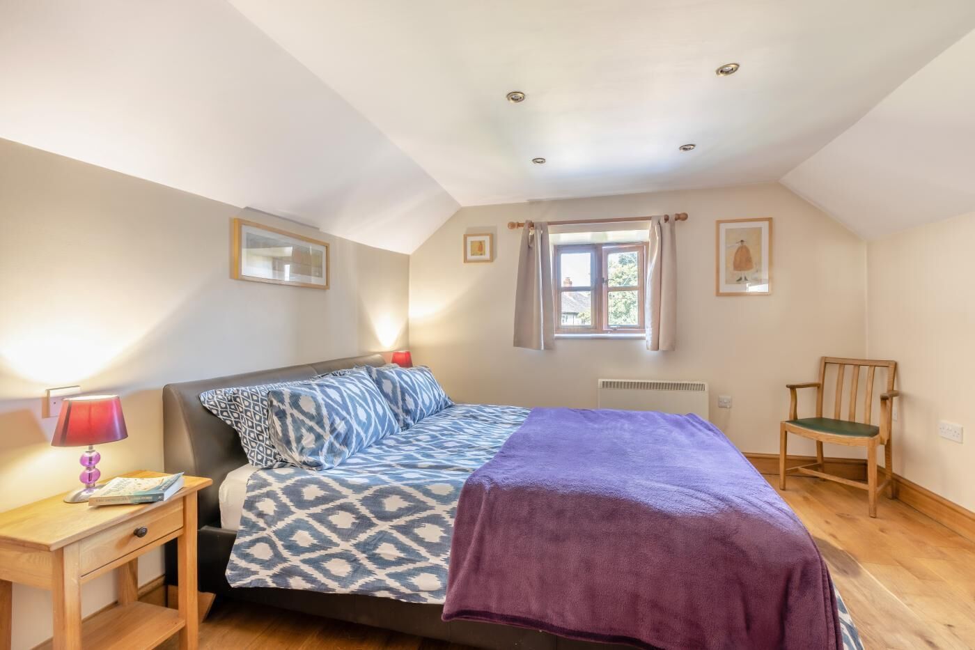 A bedroom with a bed, a nightstand, a chair, and a window.