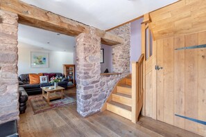 Ein rustikales Interieur mit freiliegenden Steinwänden, einer Holztreppe, einem Ledersofa und einem Bücherregal.