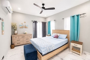 Une chambre à coucher comprenant un lit, une table de chevet, un ventilateur de plafond, une commode et un climatiseur fixé au mur.