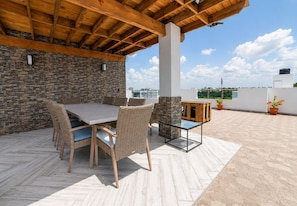 Un patio extérieur couvert, doté d’un mur en pierre, d’une table en bois avec des chaises et d’une table basse avec un plateau en verre.