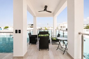 Un balcon doté d’un ventilateur de plafond, d’une rambarde en verre et offrant une vue sur le paysage urbain.