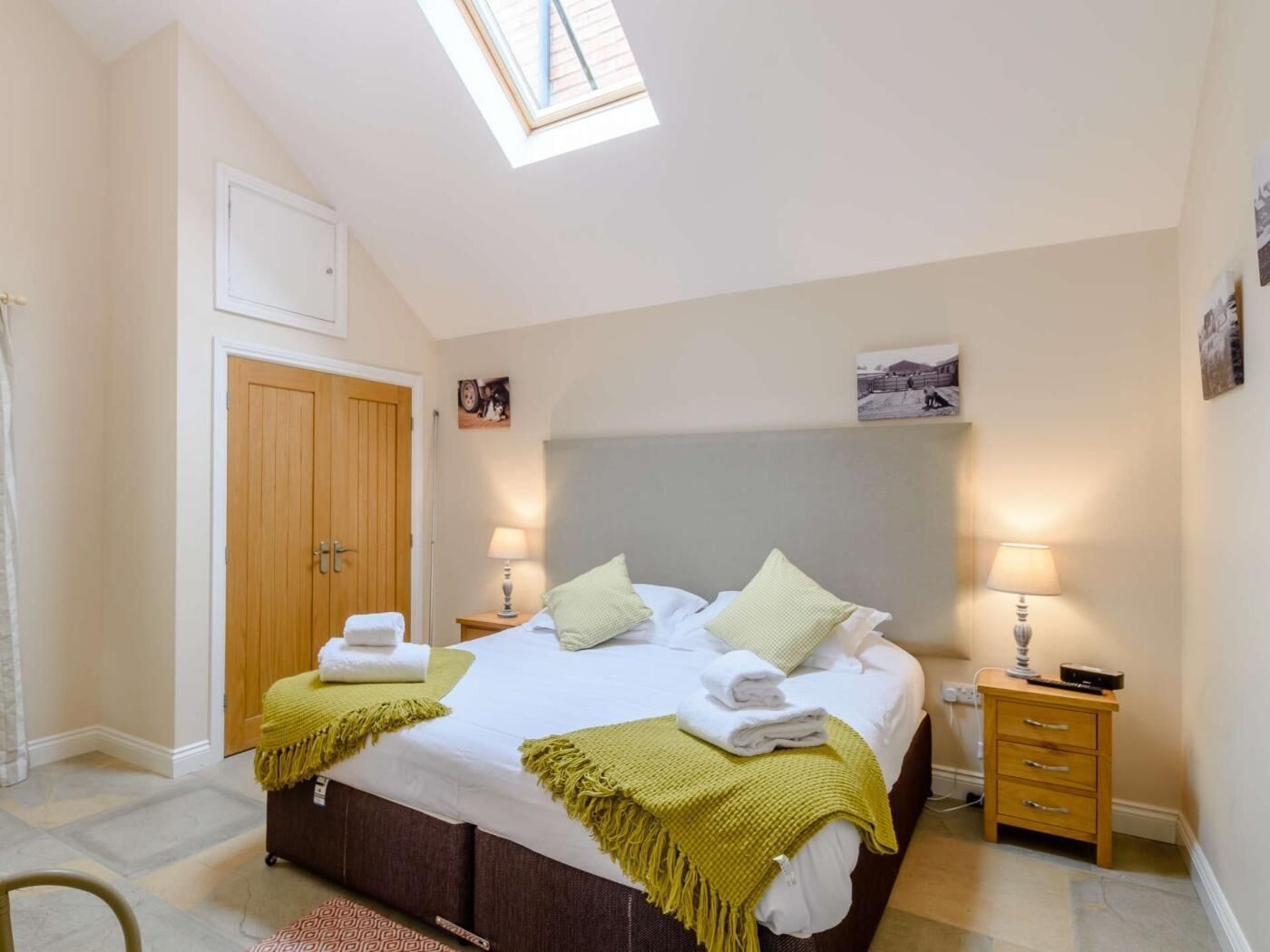 A bedroom with a bed, bedside tables, a wardrobe, a skylight, and a door.