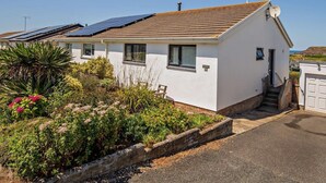 Una casa de un piso con techo inclinado, paneles solares y un pequeño jardín con diversas plantas y flores.