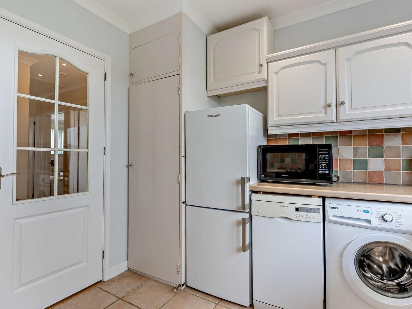 A compact kitchen with a refrigerator, microwave, dishwasher, and washing machine.