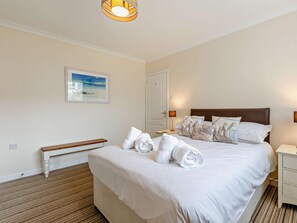 A neatly made bed with pillows and rolled towels, a bedside table with a lamp, a bench, and a framed picture on the wall.