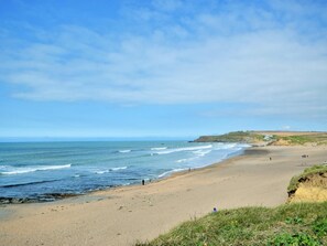 A wide sandy beach with gentle waves, a clear sky, and distant hills.