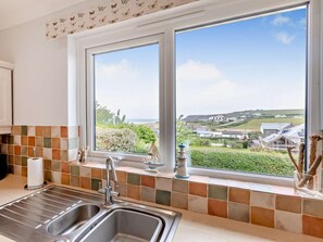 A kitchen with a large window, a tiled backsplash, and a view of a coastal landscape.