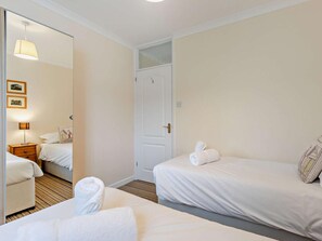 A hotel room with two beds, a wooden floor, a door, and a mirror reflecting the room.
