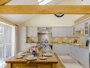 A kitchen with a long dining table set for a meal, wooden beams on the ceiling, and white cabinets.