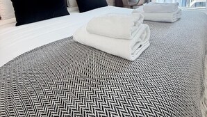 Ett hotellrum med en stor säng, en sänggavel med ett bladmotiv, ett sängöverkast med fiskbensmönster och utsikt över byggnader genom tunna gardiner.