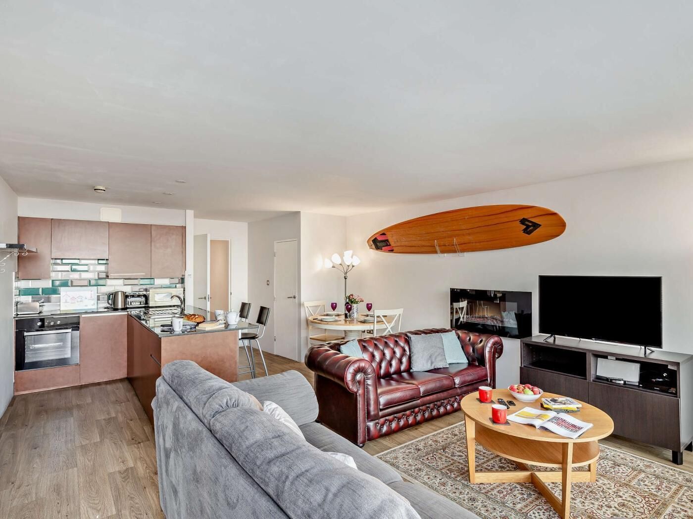 A modern living room with a sofa, a coffee table, a TV, and a kitchen area with a dining table.
