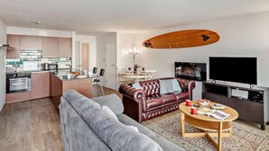 Ett modernt vardagsrum med en soffa, ett soffbord, en tv och en köksdel med ett matbord.