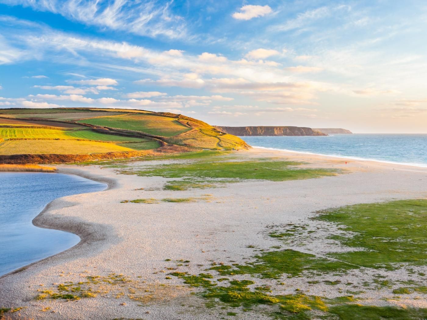 Paisagem costeira com praia arenosa, campos verdes e falésias.
