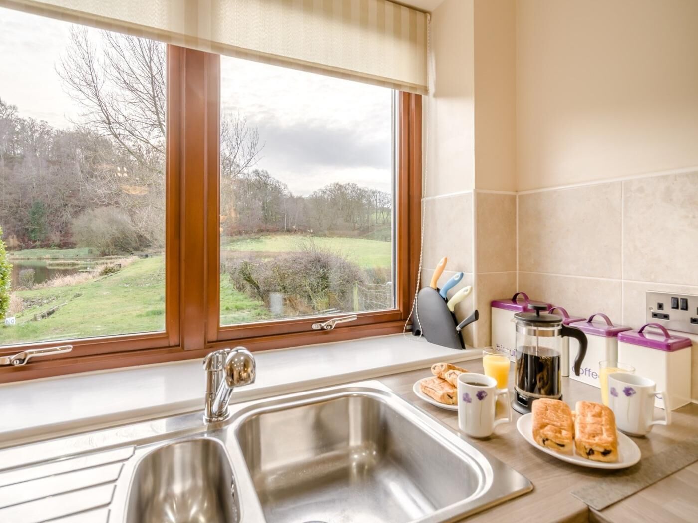 A kitchen with a large window, stainless steel sink, and breakfast items on the counter.