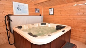 Uma cabana de madeira com banheira de hidromassagem, paredes de madeira e teto com vigas aparentes.