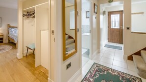 Um corredor com espelho, porta-roupas, cama e escada que leva a outro quarto.
