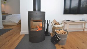 A modern room with a wood-burning stove, a bed, a TV, and a basket of firewood. - 1 Bed in Lyme Regis (oc-41563) (Uplyme)