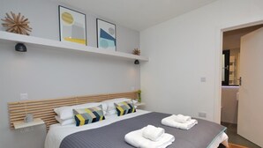 A modern bedroom with a large bed, bedside tables, and a shelf with decor. - 1 Bed in Lyme Regis (oc-41563) (Uplyme)
