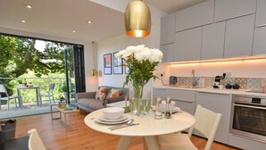 A modern kitchen with a dining area, a sofa, and a view of greenery. - 1 Bed in Lyme Regis (oc-41563) (Uplyme)