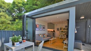A modern outdoor living space with a glass door leading to a cozy interior, a dining area, and a kitchen. - 1 Bed in Lyme Regis (oc-41563) (Uplyme)