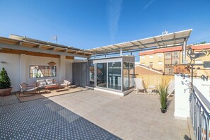 Eine Dachterrasse mit Glasveranda, Gartenmöbeln und einer Pergola mit Solarzellen.