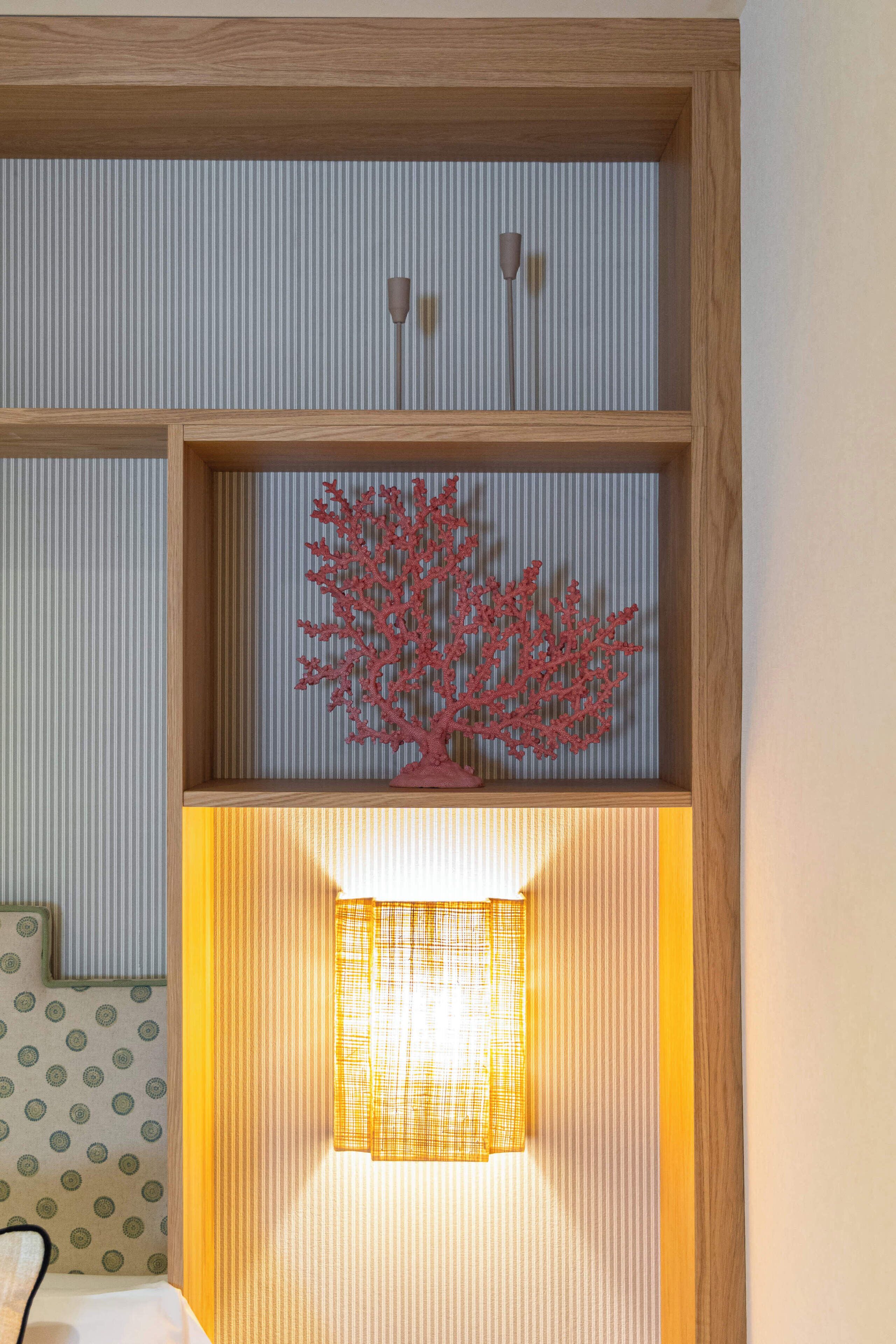 Una habitación con un estante de madera, un adorno de coral rojo y una lámpara encendida.