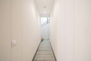 Un couloir étroit aux murs blancs, doté d’un plancher en bois et d’un escalier au fond.